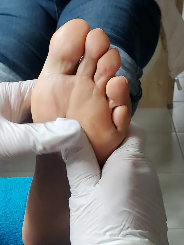 Eine Fußsohle wird mit behandschuhten Händen gehalten und für die Fußpflege kontrolliert.