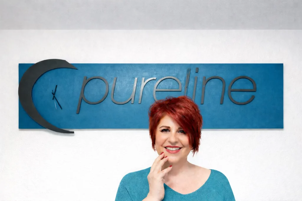 Portrait einer lächelnden Studioinhaberin vor dem Pureline Schriftzug an der Wand.