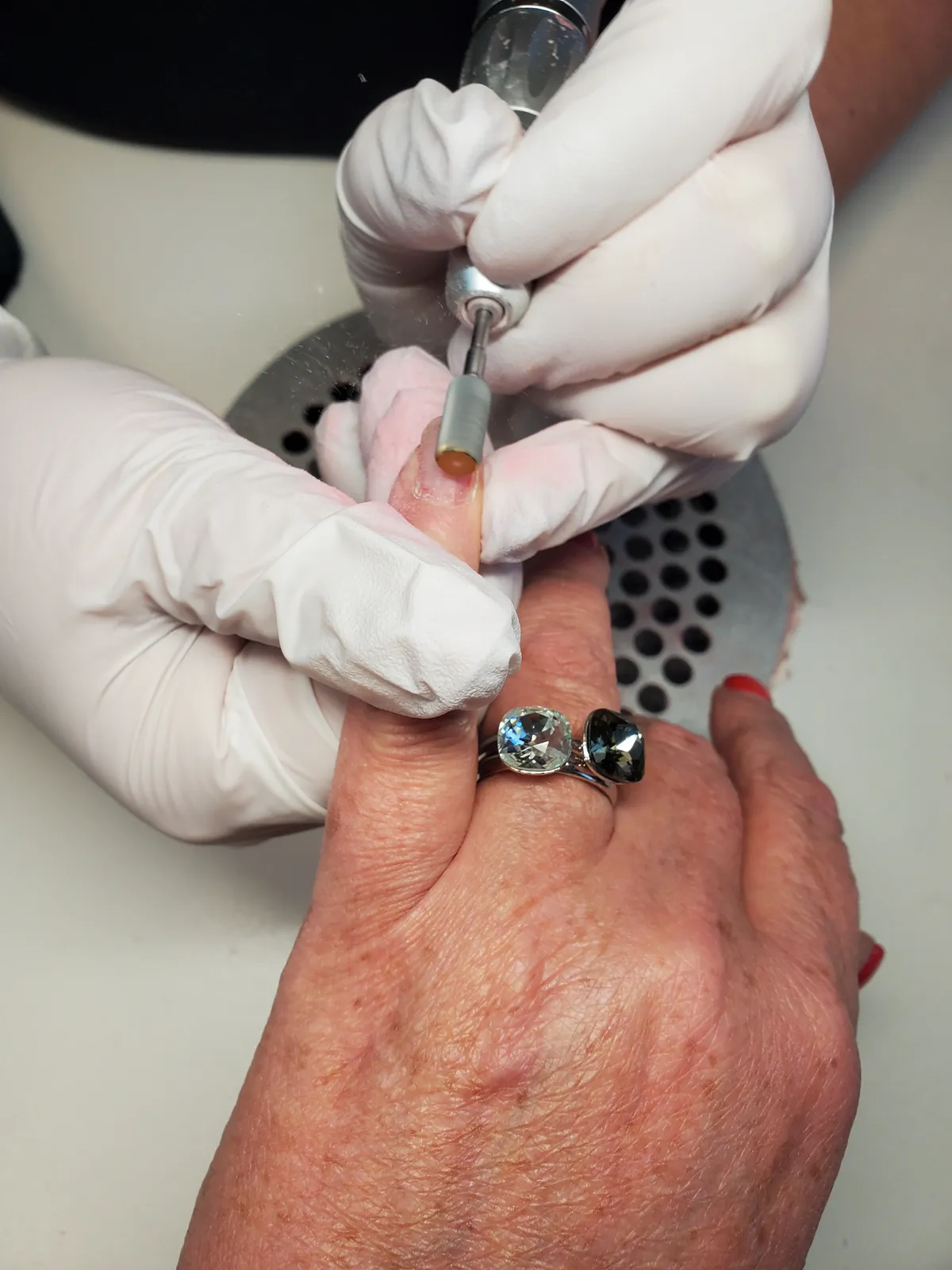 Nageldesignerin mit Handschuhen bereitet den Naturnagel mit elektrischem Fr&auml;ser vor, Nahaufnahme.