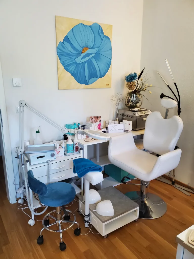 Behandlungsplatz für Fußpflege mit Stuhl, Geräten und blauem Wandbild im Studio.