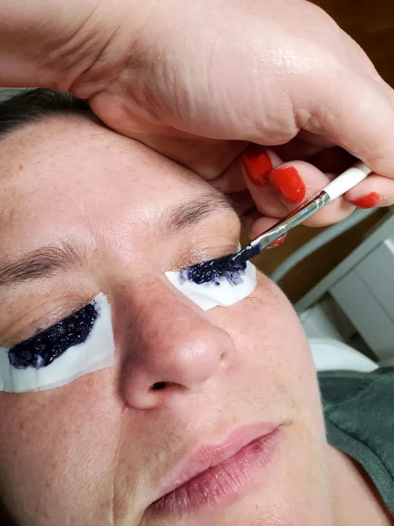 Farbe wird auf die Wimpern aufgetragen, Schutzpads liegen unter den Augen.
